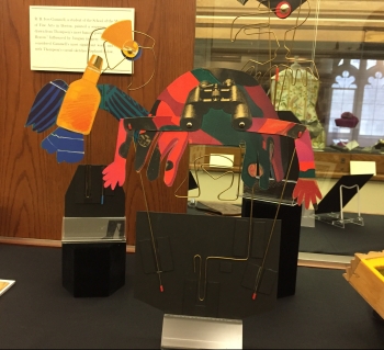 Three paper and wire puppets mounted on black cardboard to stand upright